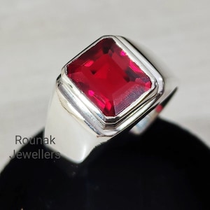 Op de afbeelding: Een zilveren ring met een vierkante rode edelsteen. De ring heeft een eenvoudig ontwerp met een gladde band.