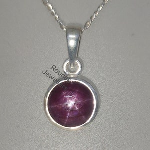 May include: A silver pendant necklace with a round, red star ruby gemstone. The ruby has a star-like pattern in the center.