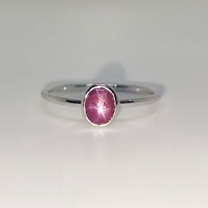 Puede incluir: Un anillo de plata con una piedra preciosa de rubí estrellado ovalada de color rosa.