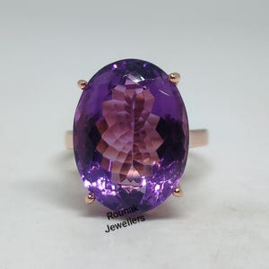 May include: A purple amethyst ring set in rose gold. The ring features a large oval-shaped amethyst gemstone.
