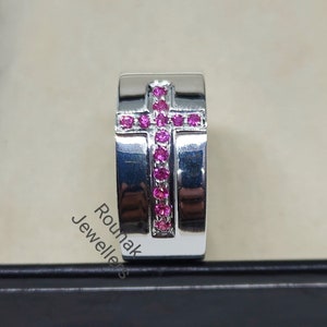 May include: A silver ring with a cross design set with pink gemstones. The ring is in a black box.