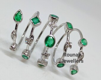May include: A silver ring with multiple emerald green gemstones and small diamonds. The ring is designed to be worn as a stackable ring. The ring is made by Rounak Jewellers.