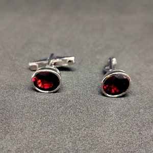 May include: A pair of silver cufflinks with oval-shaped red gemstones.