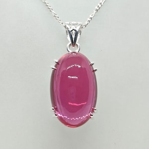 May include: A silver chain necklace with a pink oval pendant. The pendant is set in a silver bezel and has a high polish finish.