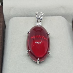 Op de afbeelding: Een zilveren hanger met een grote, ovale, rode edelsteen. De edelsteen is gezet in een zilveren bezel met vier klauwen.