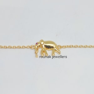 May include: A gold chain bracelet with a small elephant charm. The elephant has a pink stone for an eye.