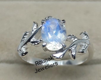 May include: A silver ring with a large oval moonstone set in a delicate leaf design. The ring is in a small box with the words "Rounak Jewellers" printed on the bottom.