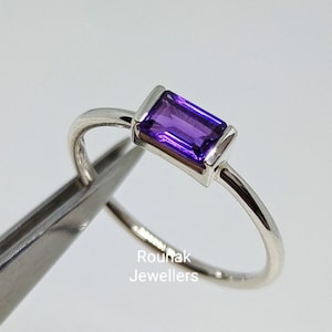 Può includere: Un anello d'argento con una ametista viola rettangolare. L'anello è tenuto da una pinzetta.