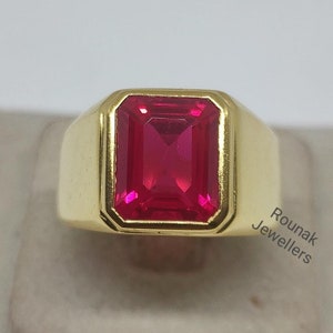 Op de afbeelding: Een gouden ring met een grote, helderrode, smaragd geslepen edelsteen. De ring is gezet in een eenvoudige, gouden band.