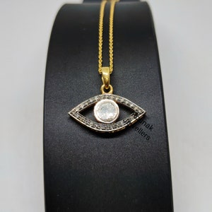 May include: A gold chain necklace with a pendant shaped like an eye. The eye is surrounded by small black diamonds and has a larger white diamond in the center.