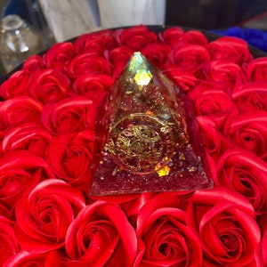 Könnte beinhalten: Ein pyramidenförmiges Harz-Ornament in Rot, Gold und Grün mit Glitter, der in das Harz eingebettet ist. Das Ornament liegt auf einem Bett aus roten Rosen.
