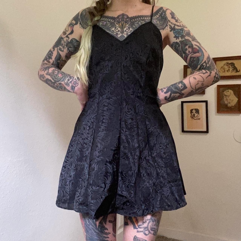 May include: A black, short, sleeveless dress with a floral pattern. The dress has a scoop neckline and a fitted bodice. The dress is made of a soft, silky fabric.