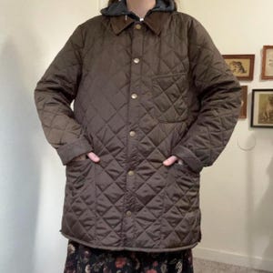 May include: A brown quilted jacket with a button-up front, a chest pocket, and two hand pockets. The jacket has a diamond pattern and a corduroy collar. The jacket is worn over a hooded sweatshirt.