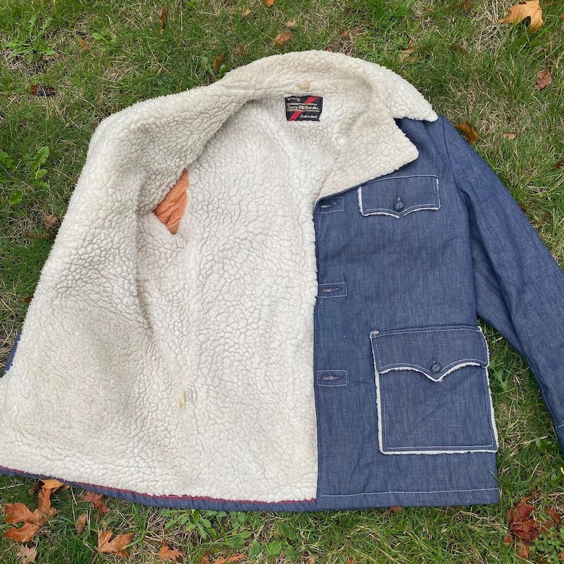 May include: A blue denim jacket with a sherpa lining. The jacket has a button closure, two pockets on the front, and a single pocket on the left sleeve. The label on the inside of the jacket reads "North Star" and "California".