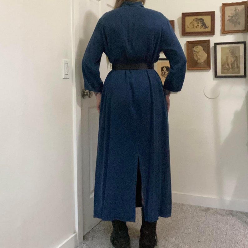 Puede incluir: Un vestido largo de color azul oscuro con cuello, una abertura en la espalda y un cintur&oacute;n negro. El vestido tiene mangas largas y un corte holgado.