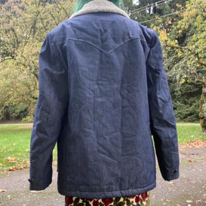 May include: A dark blue denim jacket with a sherpa collar. The jacket has a pointed yoke in the back and a button closure.