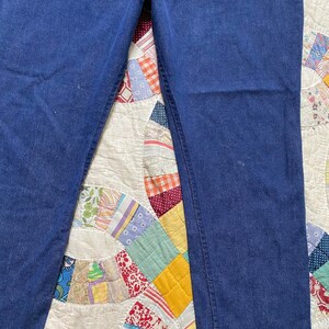 Puede incluir: Un par de pantalones vaqueros de mezclilla azul oscuro, puestos planos sobre una colcha de retazos blanca.