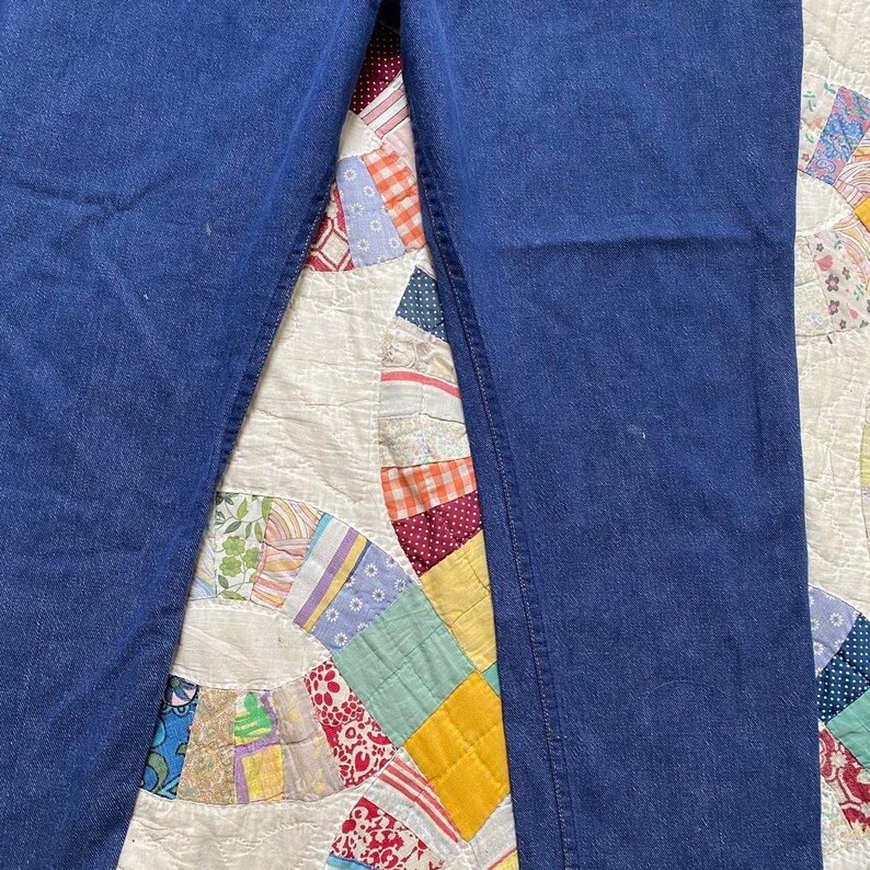 Puede incluir: Un par de pantalones vaqueros de mezclilla azul oscuro, puestos planos sobre una colcha de retazos blanca.