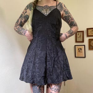 May include: A black short dress with a floral pattern. The dress has a sweetheart neckline and thin straps.