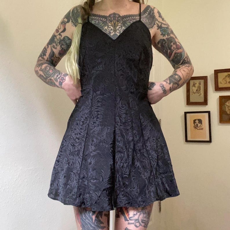 May include: A black short dress with a floral pattern. The dress has a sweetheart neckline and thin straps.