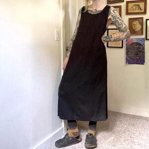 May include: A sleeveless black midi dress with a scoop neckline and a straight silhouette. The dress features a solid dark fabric that falls below the knees, paired with dark leggings, mustard-colored socks, and dark gray slip-on clogs.