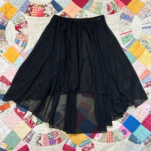 May include: A black, high-low skirt with a flowing, layered design. The skirt has a wide elastic waistband and a sheer, lightweight fabric. The skirt's hemline is shorter in the front and longer in the back.