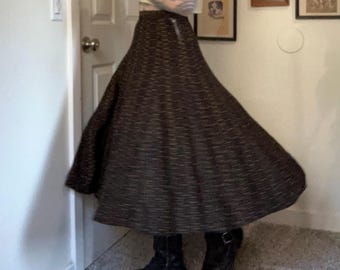 May include: A long, dark brown skirt with a textured pattern. The skirt has a wide, flowing shape and a zipper closure. The person is wearing black boots.