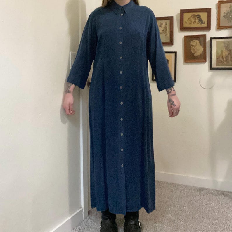 Puede incluir: Un vestido azul oscuro de manga larga con botones y cuello. El vestido tiene un corte recto y llega hasta los tobillos.