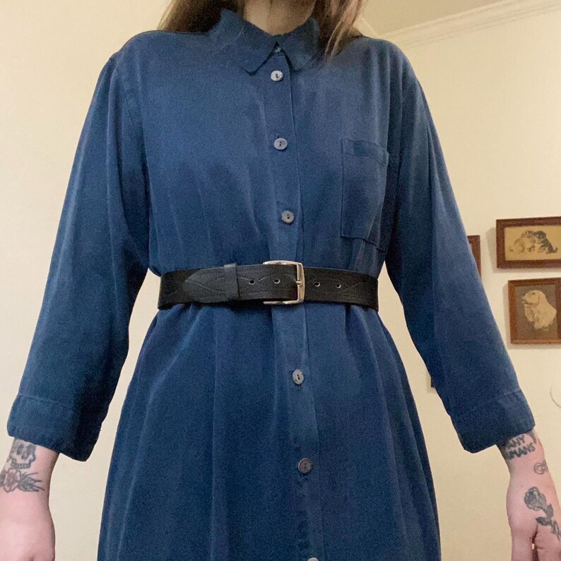 Puede incluir: Un vestido camisa azul oscuro de manga larga con botones y un cintur&oacute;n de cuero negro.
