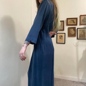Puede incluir: Un vestido largo, azul oscuro, sin mangas con escote en V. El vestido est&aacute; hecho de una tela suave y fluida.