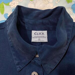 Puede incluir: Una camisa vaquera azul oscuro con una etiqueta blanca que dice "CLICK BY COLOR ME COTTON MADE IN U.S.A. L CARE ON REVERSE".