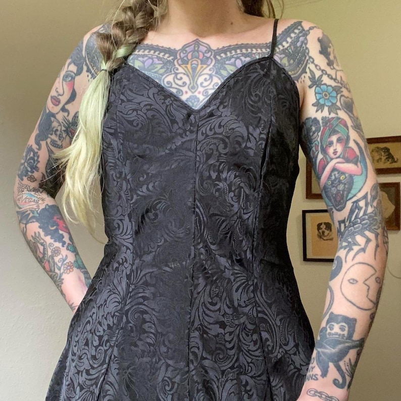 May include: A black sleeveless dress with a floral pattern. The dress has a sweetheart neckline and a fitted bodice. The dress is made of a silky fabric.