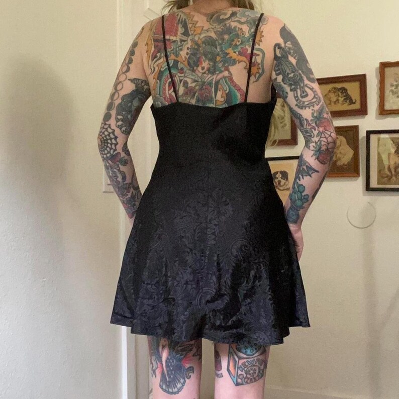 May include: A black satin dress with a floral pattern. The dress has a scoop neck and a fitted bodice. The skirt is full and flows out from the waist.