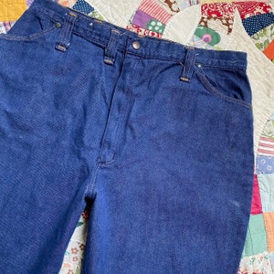 Puede incluir: Un par de pantalones vaqueros de mezclilla azul oscuro con un estilo cl&aacute;sico de cinco bolsillos. Los vaqueros tienen una pierna recta y una cintura alta.