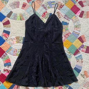 May include: A black satin slip dress with a floral pattern. The dress has thin straps and a fitted bodice.