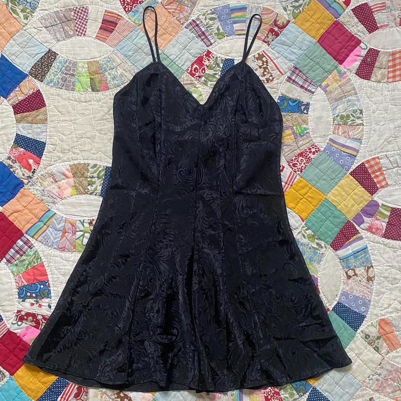 May include: A black satin slip dress with a floral pattern. The dress has thin straps and a fitted bodice.