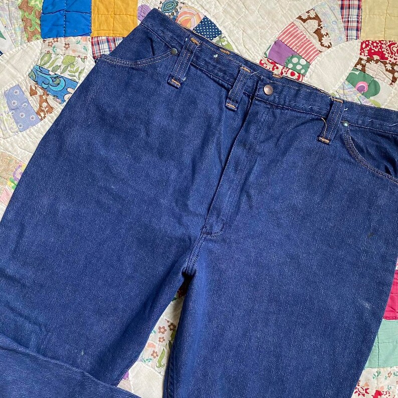 Puede incluir: Un par de pantalones vaqueros de mezclilla azul oscuro con cintura alta y pierna recta. Los vaqueros tienen un estilo cl&aacute;sico de cinco bolsillos y cierre de bot&oacute;n.