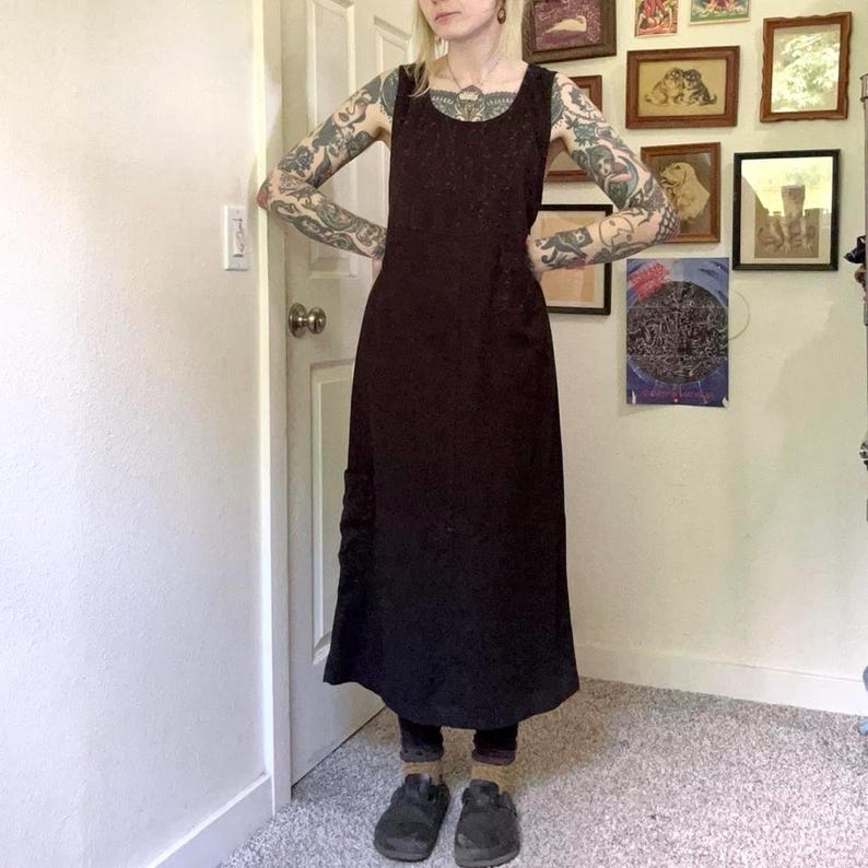 May include: A sleeveless, ankle-length black dress with a scoop neckline and a fitted bodice that transitions into a slightly flared skirt. The garment features a solid, dark fabric texture and a simple, clean-cut silhouette that falls straight.