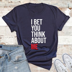 May include: A navy blue t-shirt with white text that reads "I bet you think about me". The word "me" is in red.