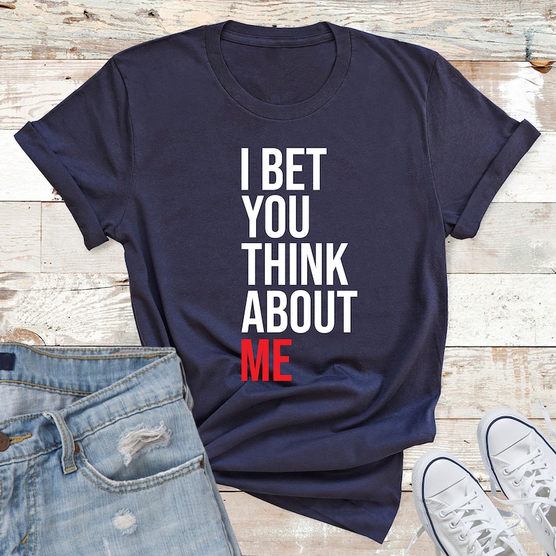 May include: A navy blue t-shirt with white text that reads "I bet you think about me". The word "me" is in red.