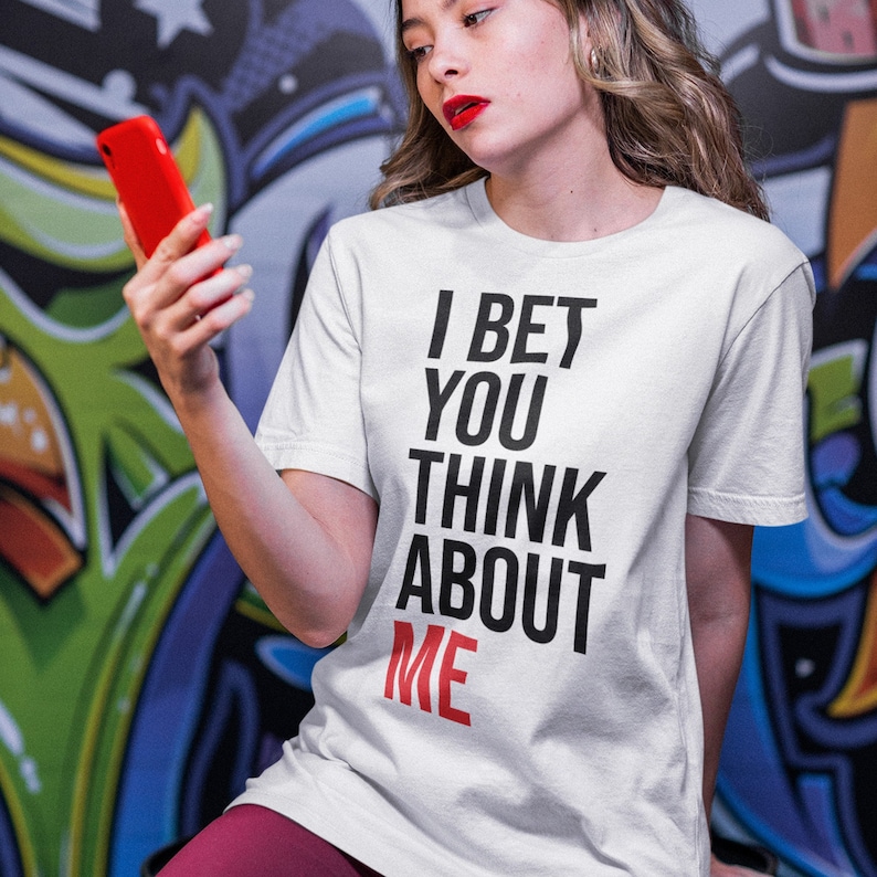 May include: White t-shirt with black text that reads "I bet you think about me". The word "me" is in red.