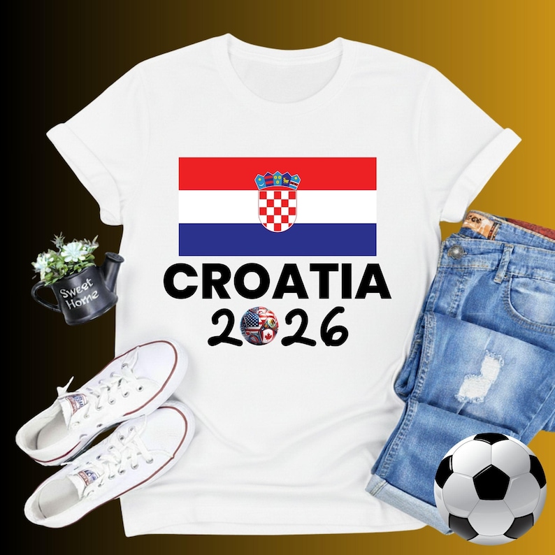 May include: White t-shirt with the Croatian flag and the text "CROATIA 2026". The image includes denim shorts, white trainers, and a football. A small decorative watering can with flowers is also present.