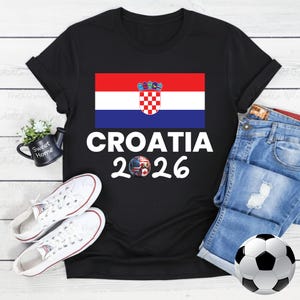 May include: Black t-shirt with the Croatian flag and the text "CROATIA 2026". A football with black and white panels is visible. White trainers and denim shorts are also in the image.