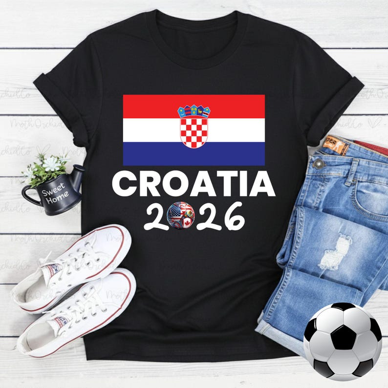 May include: Black t-shirt with the Croatian flag and the text "CROATIA 2026". A football with black and white panels is visible. White trainers and denim shorts are also in the image.
