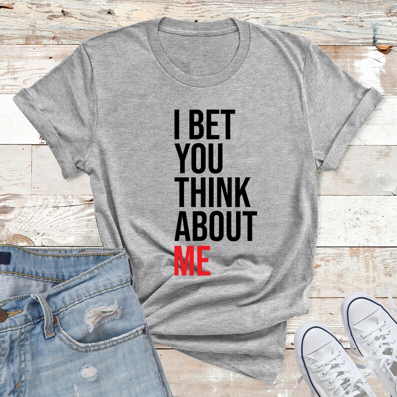 May include: A gray t-shirt with the text "I bet you think about me" printed in black with the word "me" in red.