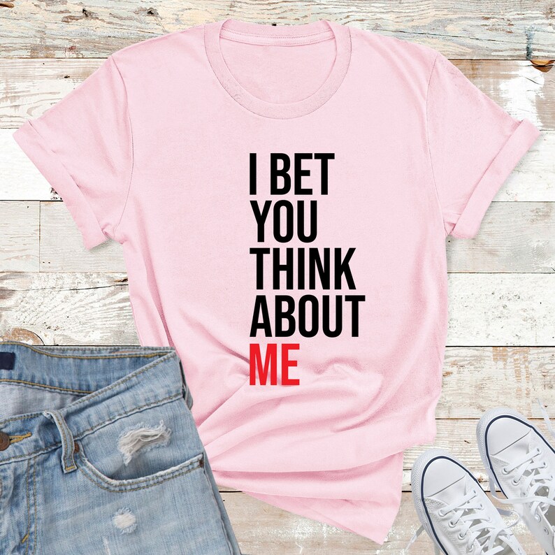 May include: Pink t-shirt with the text "I bet you think about me" in black and red lettering.
