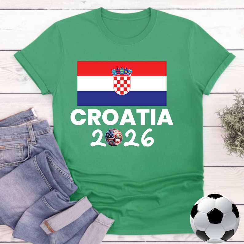 May include: Green t-shirt featuring the Croatian flag and the text "CROATIA 2026" in white. The soccer ball has the American and Croatian flags. A pair of blue jeans and a soccer ball are also in the image.