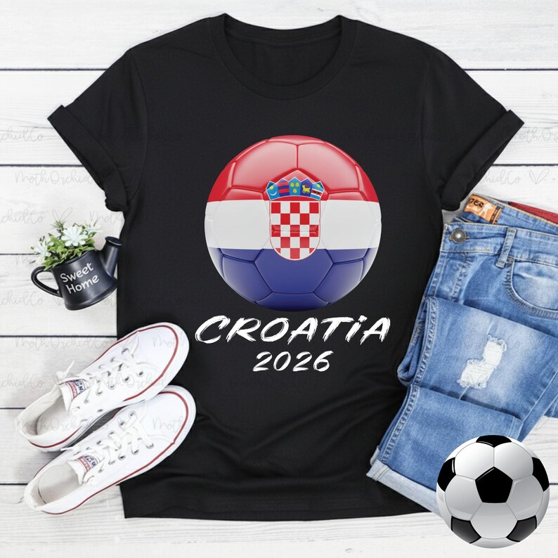K&ouml;nnte beinhalten: Schwarzes T-Shirt mit einem Fu&szlig;ball-Design der kroatischen Flagge und dem Text "CROATIA 2026". Das Bild zeigt wei&szlig;e Turnschuhe und Jeansshorts. Ein Fu&szlig;ball ist ebenfalls vorhanden.