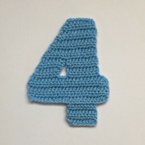 Può includere: Un numero quattro all'uncinetto di colore azzurro. Il numero è realizzato con punto basso.