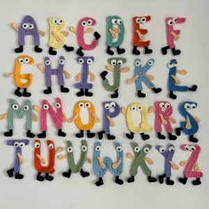 Puede incluir: Un conjunto de 26 letras tejidas a crochet, cada letra es de un color diferente y tiene ojos saltones y piernas. Las letras están dispuestas en orden alfabético.
